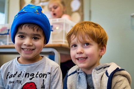 A close up of two young boys smiling. One young boy is wearing a hat that he made on the sewing machine.
